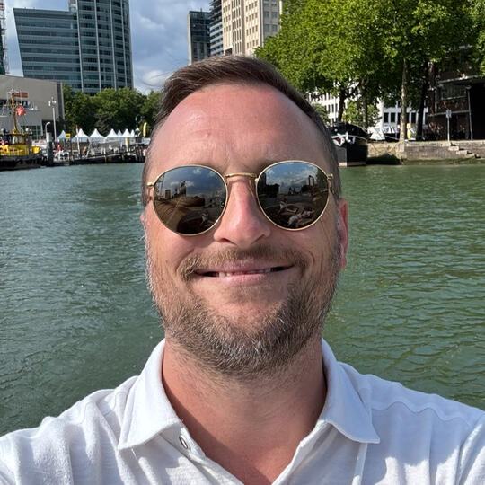Headshot of Ryan Montgomery, smiling while driving a boat in Rotterdam.